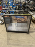 Metal wire cage on a concrete floor with industrial equipment in the background.